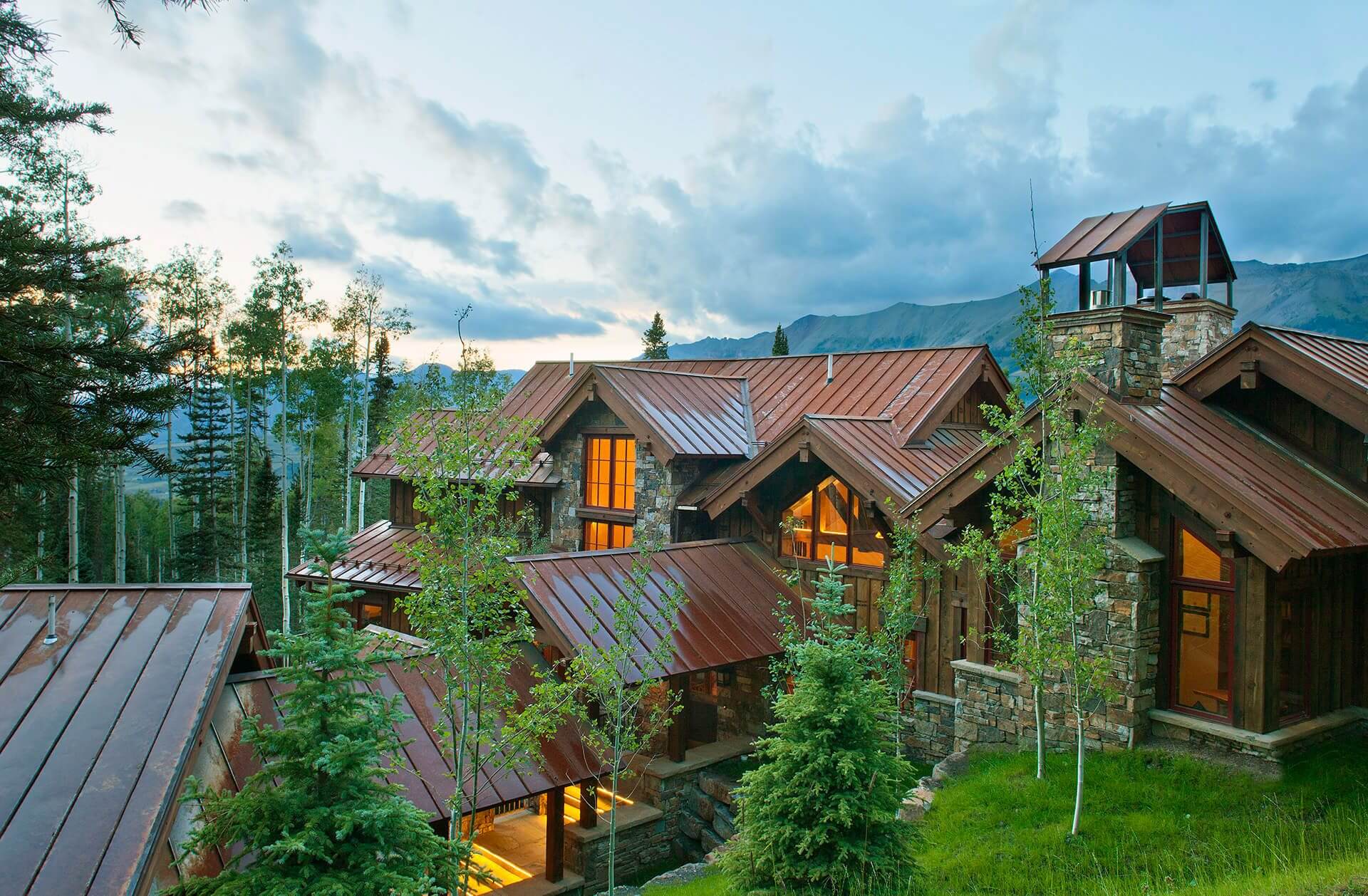 Rustic mountain cabin with copper roof at sunset.