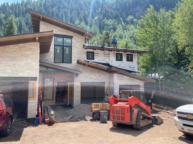 Construction site with a red excavator and a partially built house in a forested area.