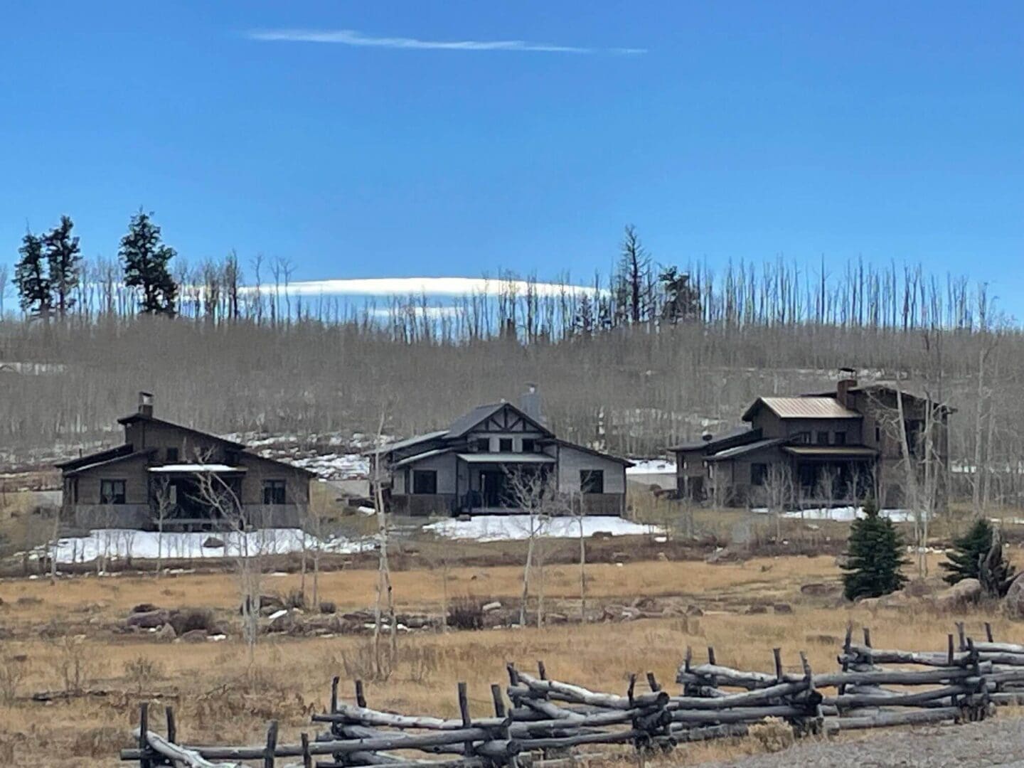 Rustic cabins near a snowy mountain under a clear blue sky.