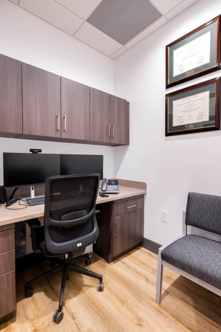A modern office workspace with computer, chair, and framed certificates.