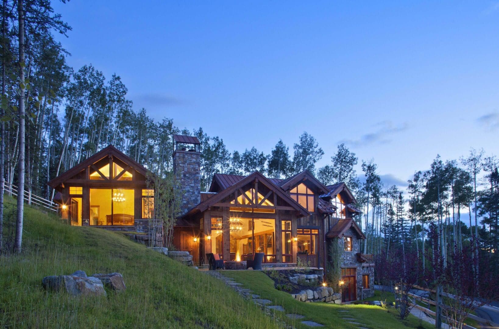 A cozy cabin illuminated at dusk in a wooded hillside setting.